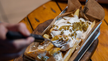 Person eating loaded french fries with cheese and jalapeños