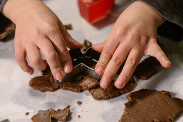 Close-up view of a child’s hands cutting out Christmas cookies from rolled dough using festive cookie cutters. A warm, cozy holiday baking atmosphere perfect for Christmas, winter, family activities