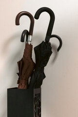 a minimalist scene featuring two closed black umbrellas placed in a contemporary umbrella stand against a light wall. The neutral tones and clean composition create a stylish, modern interior mood. Id