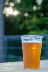 Plastic cup of cold beer on wooden table, outdoor with sunset bokeh