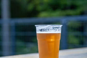 Plastic cup of golden beer with foam on outdoor wooden table in summer daylight