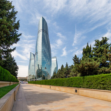 Baku, Azerbaijan - May 6, 2025: The iconic Flame Towers, stand majestically against blue sky, as viewed from Martyrs Lane. The trees in the foreground adds a touch of nature to the cityscape