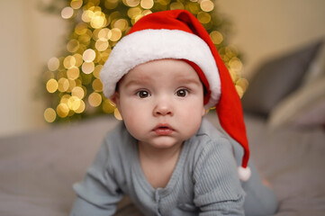 Cute baby in santa hat with christmas tree with blurred lights