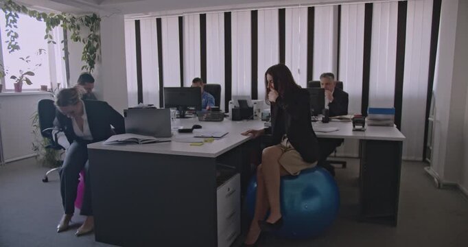 Business colleagues working and having fun in the office. They are sitting on fitness balls and enjoying their workday.