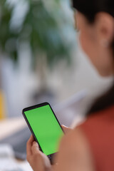 Asian woman small entrepreneur using a smartphone with a green screen mockup in her home office, checking digital content while managing her business tasks
