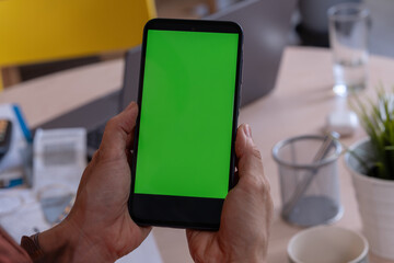 Asian woman small entrepreneur using a smartphone with a green screen mockup in her home office, checking digital content while managing her business tasks