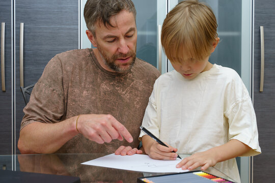 A father helps his young son with a drawing lesson at home. Parent teaching a child creative skills