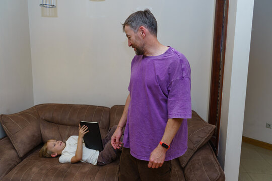 Father talking to his son using a tablet at home. Parenting and screen time in a family setting