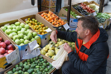 Man with a reusable bag choosing fresh quince at an outdoor farmers market. Healthy food shopping