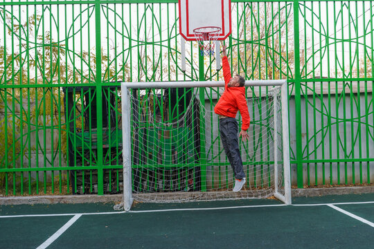 Man jumping to a basketball hoop on an outdoor court. Athlete playing inside a soccer goal