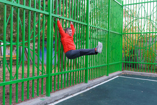Active middle-aged man performing a hanging leg raise. Street workout and fitness concept - Powered by Adobe