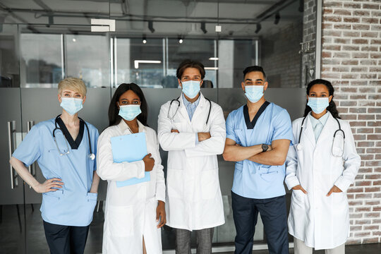 International medical team male and female doctors in workwear and face masks having team-building, posing together while COVID-19 pandemic at clinic. Professions, occupations, healthcare concept - Powered by Adobe