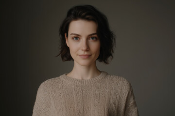 A close-up portrait of a serene young woman with short dark hair and blue eyes, wearing a beige knitted sweater. Natural beauty, calm expression, minimal aesthetic concept.