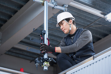 天井が近い高所の足場で単管パイプを固定するクランプなどの施工作業　鳶職や作業員のイメージ　レンチで締め