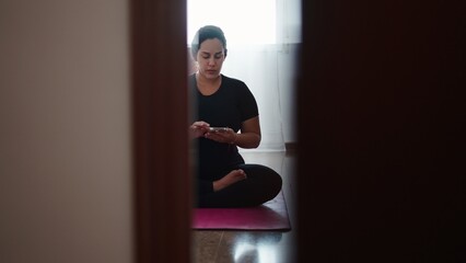 Pregnant woman practicing yoga, holding phone, relaxing in lotus position