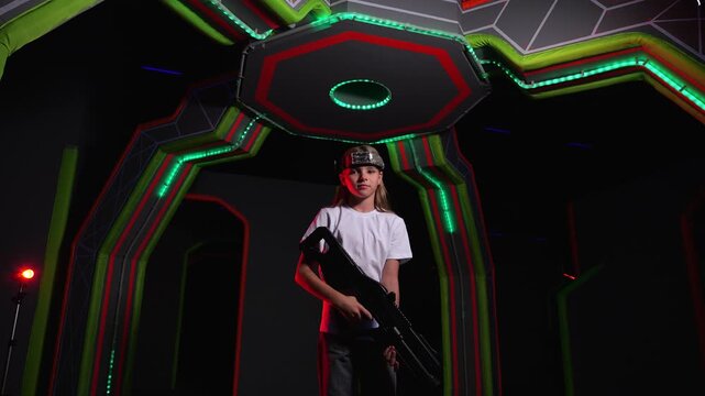 Portrait of a teenage girl with a laser weapon and a marker on her head in a laser tag room, neon stripes on the walls and ceiling. A modern laser tag game area.