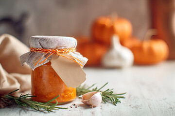 Delicious homemade pumpkin preserves with garlic, displayed in a jar on a wooden table with pumpkins in the background