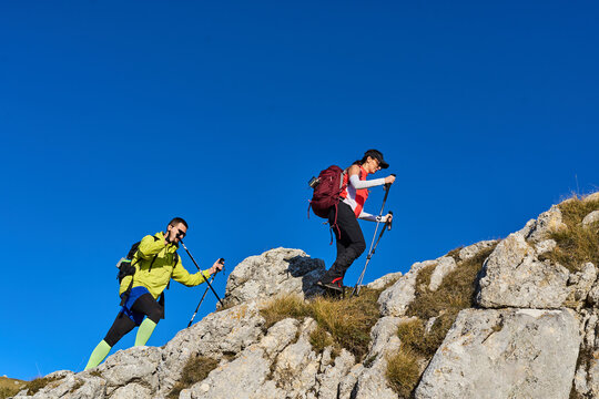 Two hikers climbing a rocky trail under a clear blue sky in the mountains during daytime