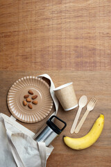 Eco-friendly picnic setup with reusable cutlery, paper cup, stainless bottle, banana, and almonds on wooden background. Perfect for zero waste, healthy lifestyle, and sustainability concepts.