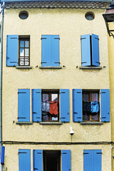 Three-story residential building in Sisteron, France, with a yellow facade and blue shutters on six windows. Clothes hang from a line across two open windows on the second floor