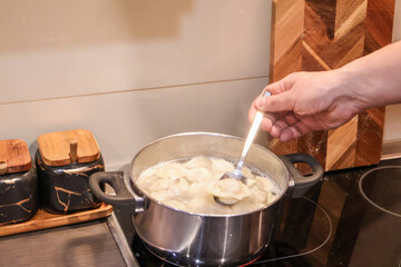 Man cooking dumplings on the stove, adding spices and stirring, teamwork and male participation in household tasks. A warm and authentic family cooking together at home. Real domestic life.
