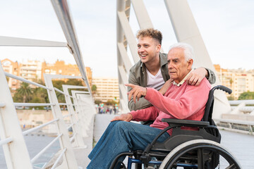 A smiling grandson sharing a tender moment with his grandfather in wheelchair on an urban bridge