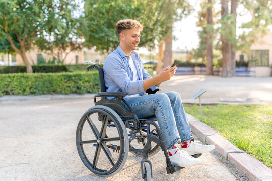 Young man with disability in wheelchair enjoying time outdoors using phone in park