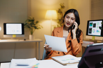 Asian businesswoman working late managing paperwork and phone call