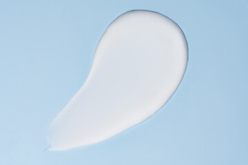 Texture of white cream on blue background. Smear of moisturizer close up. Lotion swatch. Beauty skin care product smear smudge. SPF sunscreen cream sample on blue background