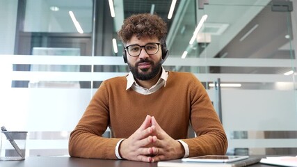 Webcam view. Confident businessman in a headset talking on a video call looking in camera sitting in modern office. Male professional has a business meeting. Manager speaks at remote online conference - Powered by Adobe