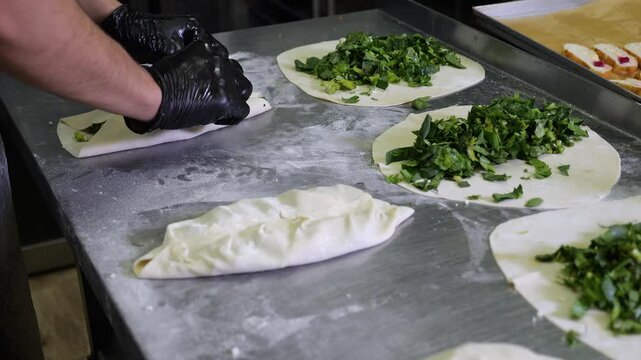 Close-up of the cook cooking tortillas with greens, she forms a tortilla and pinches the edges. Traditional Asian cuisine. Gozleme, kutaby. The concept of catering and takeaway food.
