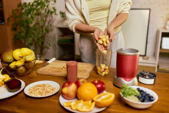 Woman adding chopped fruit into blender cup while preparing homemade smoothie. Concept of healthy meal prep guides, recipe tutorials, nutrition storytelling, wellness branding.