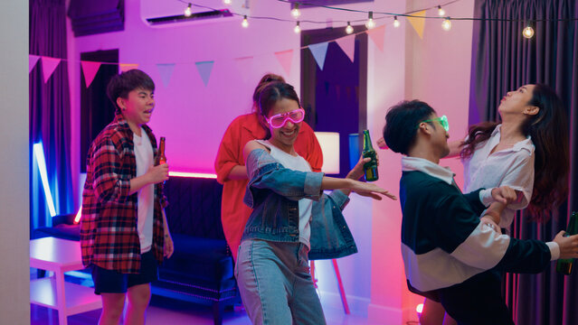 Diverse group multiethnic young adult Asia friend wear futuristic neon glowing glasses dance and drink alcohol beer fun hangout party in living room night indoor home. Disco lights illuminating house. - Powered by Adobe