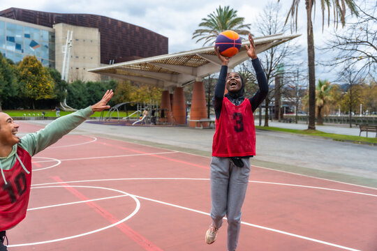 Woman in hijab shooting basketball on court