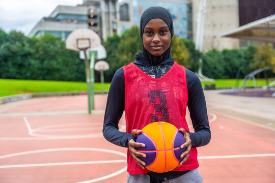 Young muslim woman holding basketball on court - Powered by Adobe