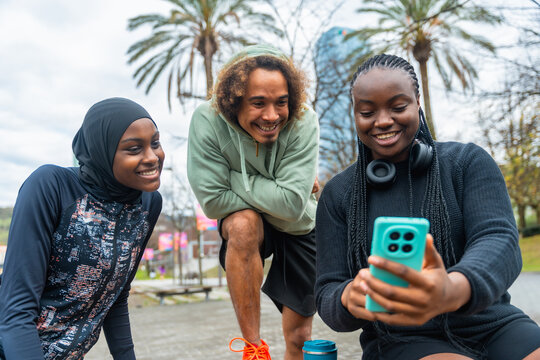 Diverse friends enjoying social media content on smartphone outdoors - Powered by Adobe