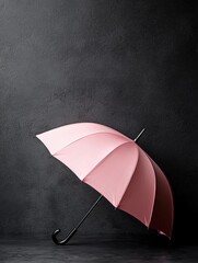 Photograph of a pink umbrella against a dark grey wall. the umbrella is open, with the handle facing upwards and the canopy slightly tilted to the side.