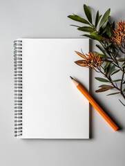 Flat lay of a white notebook with a spiral binding on the left side. on the right side of the image, there is a branch with orange flowers and green leaves.