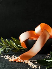 Close-up of an orange ribbon tied in a bow on a black background. the ribbon is lying on the right side of the image, with a small black bowl on the left side.