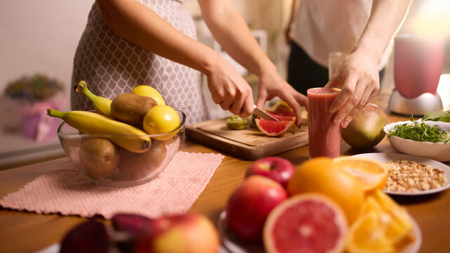 Couple preparing fruit for smoothies with fresh produce arranged on kitchen table. Concept of cooking classes, wellness lifestyle promotion, food influencer content, nutrition education.