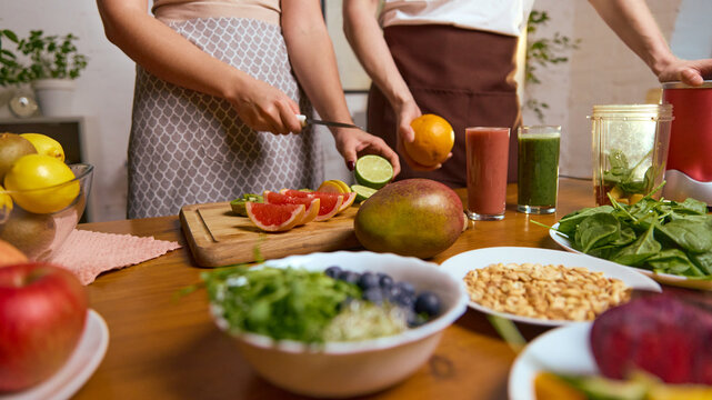 Slicing citrus and kiwi while smoothies stand among fresh produce on table. Concept of recipe creation, healthy cooking lessons, beverage tutorials, wellness food branding.