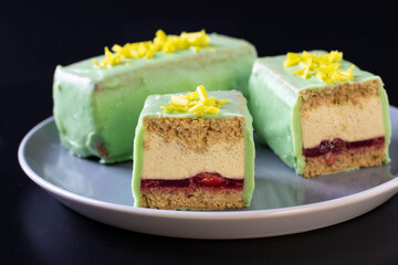 Sliced mousse desserts with almond biscuit, cherry coolie and banana mousse covered gourmet green chocolate glaze