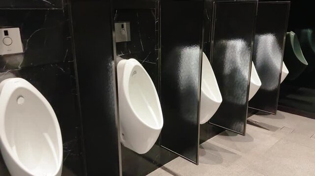 Modern row of urinals in public restroom with black marble partitions