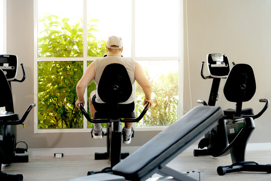 A man in athletic wear works out on an elliptical trainer in a bright and modern gym. His intense expression shows determination and focus as he continues his fitness routine.

