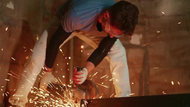 man using angle grinder cutting steel, sparks flying across concrete floor, bent worker wearing goggles and gloves, focused motion, warm orange light, gritty industrial mood