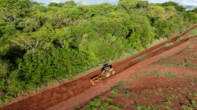 Tractor with agricultural implement plowing land next to riparian forest