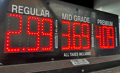 A fuel station shows the current gas prices for regular, mid grade, and premium fuel types in bright, illuminated digits.