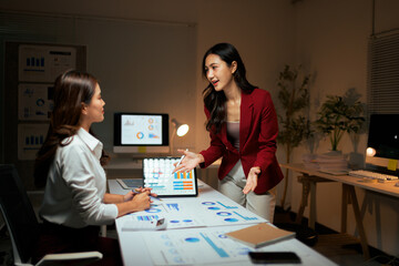 Businesswomen discussing data analysis charts late at night