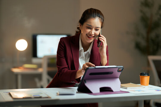 Asian businesswoman multitasking, talking on phone and using tablet - Powered by Adobe