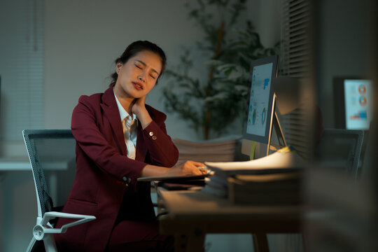 Asian businesswoman experiencing neck pain working late in office - Powered by Adobe